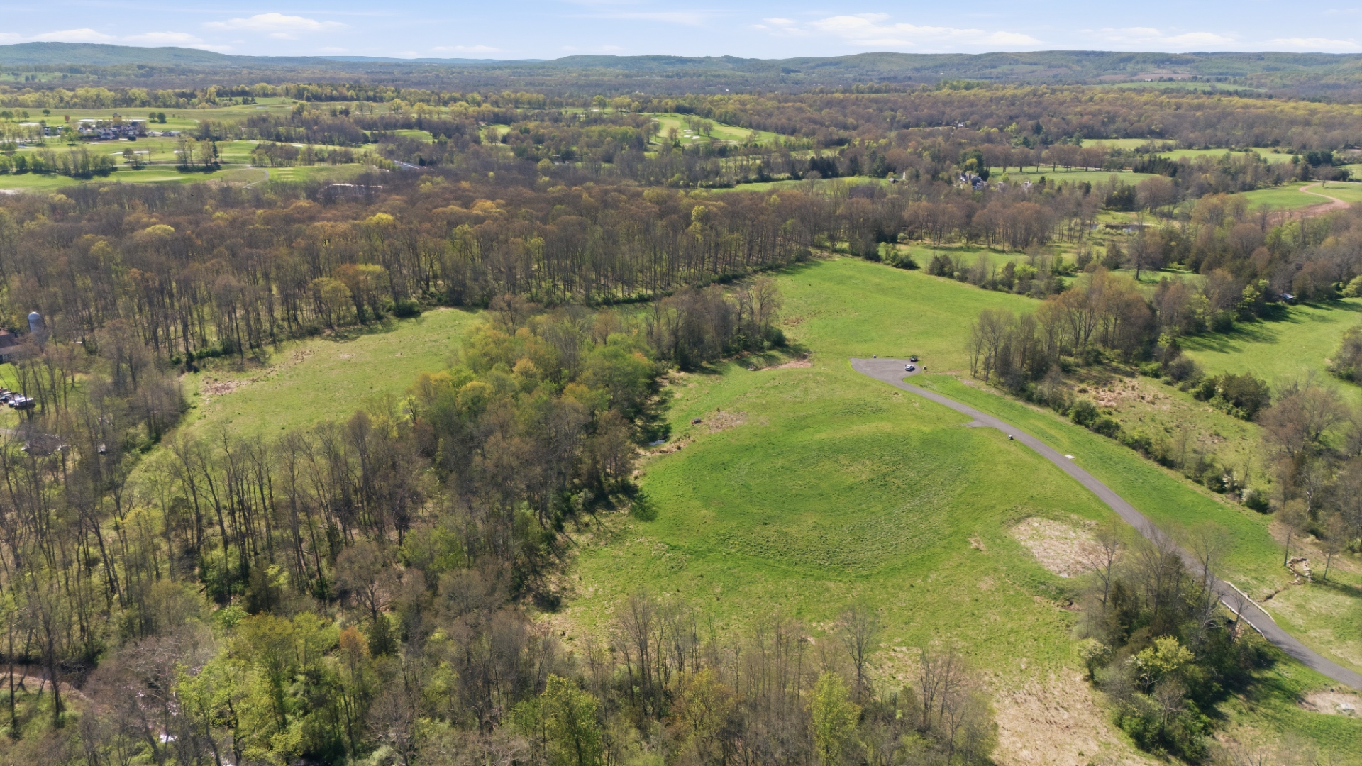 Elevated aerial of the tract's wooded ridge and cleared building envelopes with distant Somerset County farmland