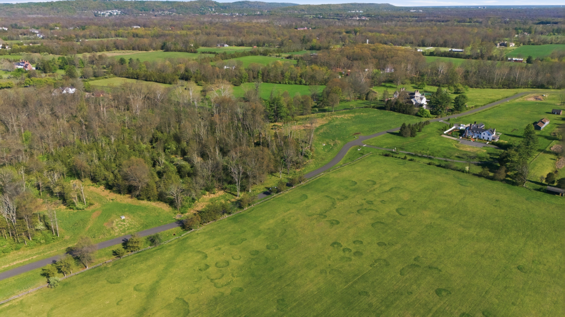 Aerial view of the Bedminster Farms land offering at 1310 Lamington Road, with a paved private roadway winding past open green pasture and an existing estate residence